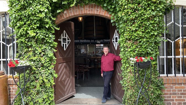 Bild: Der Hausherr im bl&uuml;henden Innenhof vor der rustikalen Niederlage