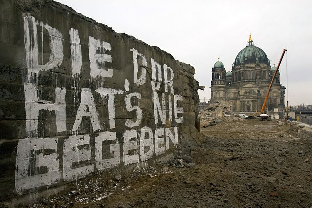 Bild: Die Aufnahme von Arno Burgi stammt aus dem Jahr 2008. Es zeigt eine Mauer der Br&uuml;cke Rathausstra&szlig;e auf der in wei&szlig;er Farbe geschrieben steht Die DDR hat&acute;s nie gegeben. Im Hintergrund ist der Berliner Dom zu sehen, dazwischen die Brache, auf der einst der Palast der Republik gestanden hat. Das Foto darf bis zum 31. Dezember 2025 im Rahmen der Berichterstattung &uuml;ber die Ausstellung Aufarbeitung. 
