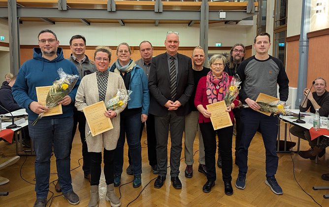 Marcus Reichhardt (links), Michaela Aquillon (3.v.li.), Karin Hafermalz (3.v.re.) und Ronny Kuhmann (rechts) nahmen ihre Auszeichnungen als Gewinner des B&uuml;rgerbudgets 2025 von B&uuml;rgermeister Steffen Grimm (5.v.re.) und den Fraktionsvorsitzenden Lars Boltze, CDU (2.v.li), Dagmar Sonneck, SPD (4.v.li.). Holm Suffa, AfD (hinten Mitte), Tobias Schneegans, VS (4.v.re.) und Jens Koschinek, Die Linke (2.v.re.) entgegen. (Foto: Janine Skara)