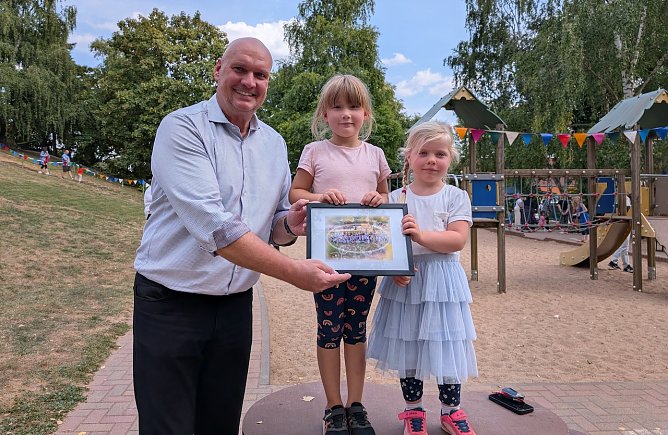 Marlen und Magdalena &uuml;berreichten B&uuml;rgermeister Steffen Grimm ein Andenken zum 50. Geburtstag der Kita Pusteblume. (Foto: Janine Skara)
